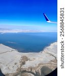 View of Salt Lake City, Lake from the window of a plane above the ground. Shows the blue skies, the wing of the plane, and the Salt Lakes below. 