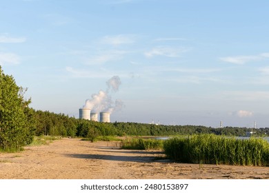 A view of a sandy beach and a distant nuclear power plant with smoke plumes