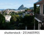 View of Santa Teresa, Rio de Janeiro, Sugarloaf Mountain in the distance, balcony overlooking dense vegetation and urban structures, iconic landscape and urban juxtaposition