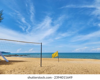 A view of the sea during the day with a bright blue sky, a yellow flag warning people to be careful while playing in the sea, and a net for playing beach sports such as volleyball. or other exercise.  - Shutterstock ID 2394011649