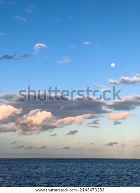 View from\
the sea of a full moon over fluffy\
clouds