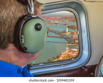 View From A Sea Plane Window Flying Over Sydney Harbour Australia. A Tourist Man Looks Out Wearing Ear Defenders.