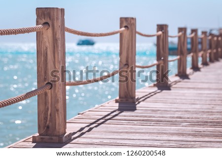 View at the sea from the wooden pier with posts and ropes with sparkling sea water