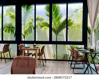 A view of a section of a café with small palm trees outside the windows.