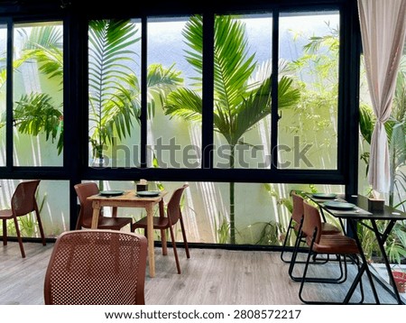 A view of a section of a café with small palm trees outside the windows.