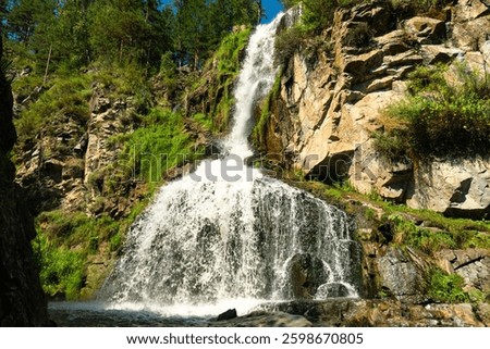 View of the seething stream of falling water of the Kamyshlinsky waterfall on a sunny summer day in the Altai Republic, Russia