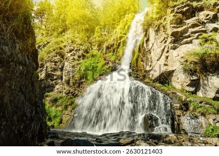 View of the seething stream of falling water of the Kamyshlinsky waterfall on a sunny summer day in the Altai Republic, Russia