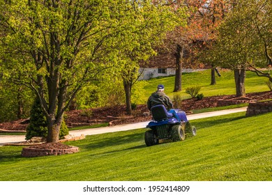 View Of Senior Man Mowing His Steep Front Yard On Riding Lawn Mower In Spring