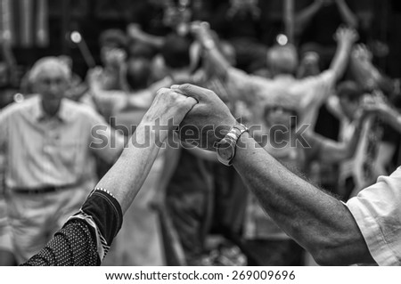 View of senior people holding hands and dancing national dance Sardana at Plaza Nova, Barcelona, Spain. It is a type of circle dance typical of Catalonia