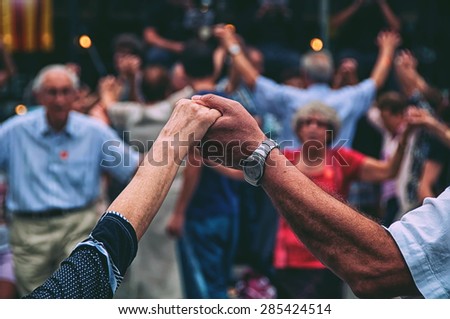 View of senior people holding hands and dancing national dance Sardana at Plaza Nova, Barcelona, Spain. It is a type of circle dance typical of Catalonia. Toned photo