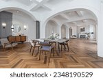 a view of a set dining table in a chic expensive bright interior of a huge living room in a historic mansion with arched arches, columns and white walls decorated with ornaments and stucco.
