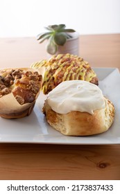 A View Of Several Breakfast Pastries On A Plate, Featuring A Blueberry Muffin, Cinnamon Roll And A Scone.