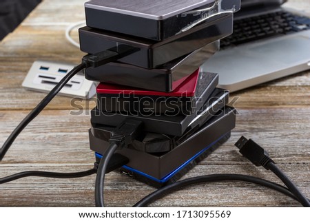 A view of a several external hard drives stacked together in front of a laptop computer on a wooden surface.