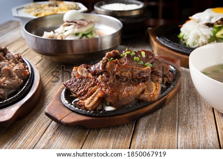 A view of several Korean entrees prepared on a wooden table surface, featuring galbi.