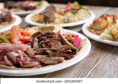 A View Of Several Mediterranean Entrees On A Wooden Table Surface, Featuring Beef Shawarma.