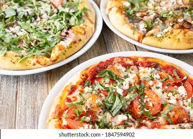 A View Of Several Rustic Pizzas On A Wooden Table Surface.