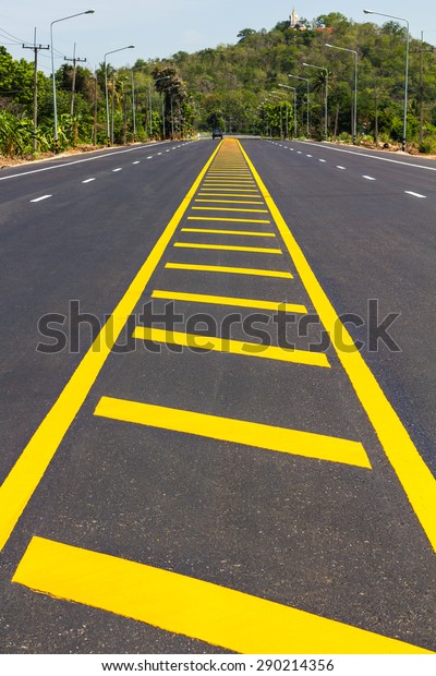 View shaped yellow stripes that divide the\
paved road that leads to a small\
hill.