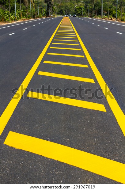 View shaped yellow stripes that divide the\
paved road that leads to a small\
hill.