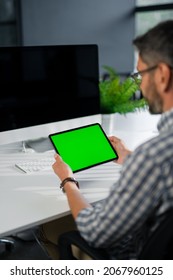 View From The Shoulder Of Man Using Hand Gestures Tap On Green Mock-up Screen Digital Tablet Computer In Landscape Mode Sitting At The Desk In The Office