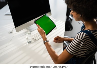 View From The Shoulder Of Woman Holding And Using Hand Gestures Swipe Up On Green Mock-up Screen Digital Tablet Computer Sitting At The Desk. Browsing The Internet. Background Office.