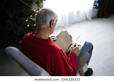 View from shoulders on widower holding photo-album looking photos and remembering deceased wife on Christmas morning. Close-up - Powered by Shutterstock