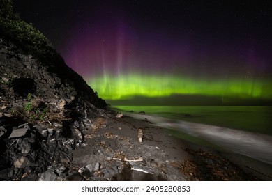 view of the side of a beach with waves and a green and purple aurora in the sky
