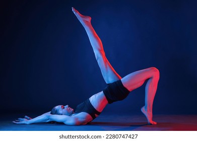 View from the side, lying down on the floor. Beautiful muscular woman is indoors in the studio with neon lighting.