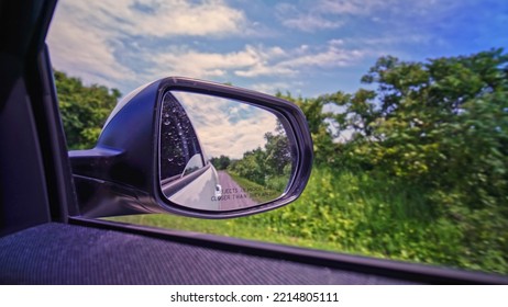 View In The Side Mirror Of A Car While Driving At Rural Country Side Bumpy Road. Back View Side Vehicle Mirror Look Of The Passenger. Travel And Trip. Drivers License Lessons And Education. Test Drive