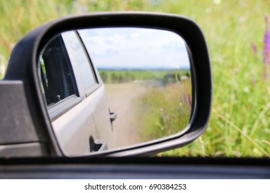 View in the side mirror when driving a crossover at a high speed on a picturesque dusty field road in the summer