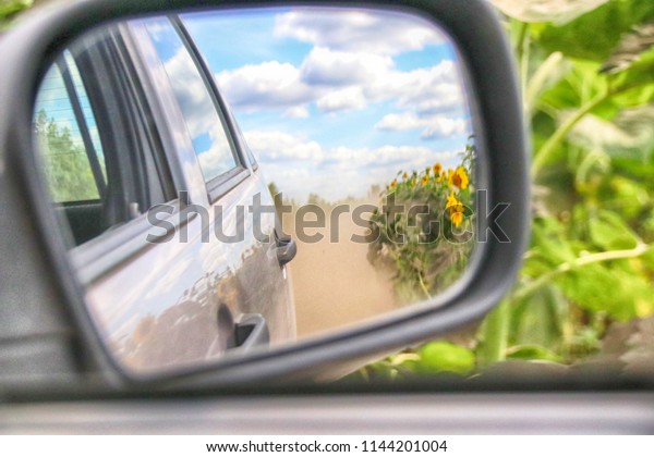 View in the side mirror when driving a
crossover at a high speed on a picturesque dusty field road along
the sunflower field in the sunny summer
day