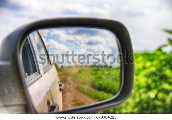 View in the
side mirror when driving a crossover at a high speed on a
picturesque dusty field road in the
summer