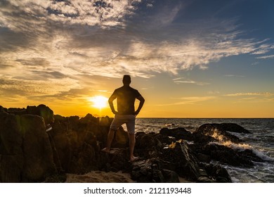 View  silhouette of a man standing on a rock and facing the sea at sunset,The warm atmosphere and the orange glow of the sun.