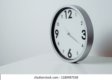 A View Of A Silver, Large Wall Clock. Side View Of A Clock Showing The Time Lying On A White Table. The Concept Of Passing Time, Ending Work, Returning To School And Work Tasks.