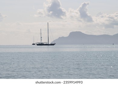 View of the silver-grey shimmering sea, the grey mountain ranges of the Tramuntana mountains in the background and the dark silhouettes of sailing ships in the distance - Powered by Shutterstock