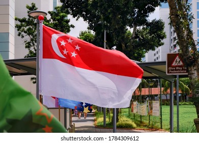 View Of Singapore Flag Waving In The Wind On Bright Sunny Day In HDB Neighbourhood. Selective Focus