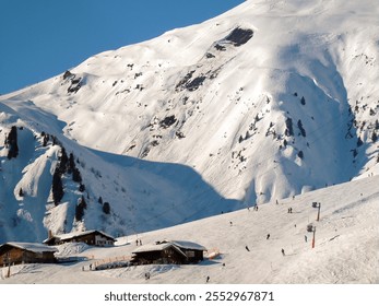 View of a ski slope covered with snow and houses of a tourist resort built on a mountain slope. Bright blue sky in the background - Powered by Shutterstock