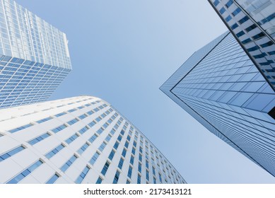 The view of the sky between three skyscrapers at noon. Modern office buildings in the financial district. Glass towers in downtown of the city. A cluster of tall buildings.