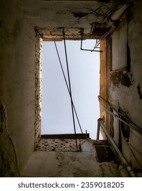 A view of the sky through a hole in the ceiling of an old building. The sky is blue and there are clouds in the sky. The hole is surrounded by peeling paint and old brickwork.