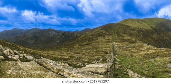 A view from Slieve Donard in the Mourne Mountains, Northern Ireland, featuring the Mourne Wall crossing rugged terrain. The landscape is framed by rolling hills and Dramatic sky. - Powered by Shutterstock