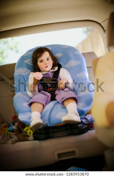 View of a small girl eating ice cream whilst sitting\
in a car.