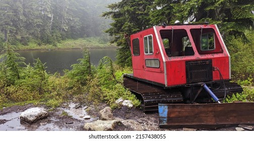 A view of a small lake surrounded by pine trees and a skidder on the shore in British Columbia