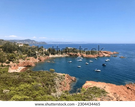 A view of a small rocky cove adorned with vegetation, brown rocks. The clear blue water fills the bay, inviting exploration and relaxation. The scene exudes tranquility and natural beauty.