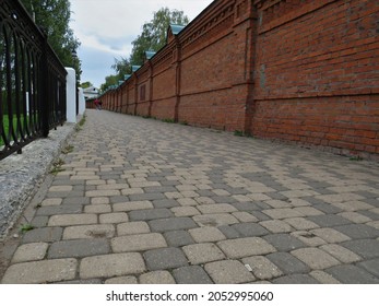 view of a small street covered with cobblestones along which there is an old brick wall on an autumn cloudy day