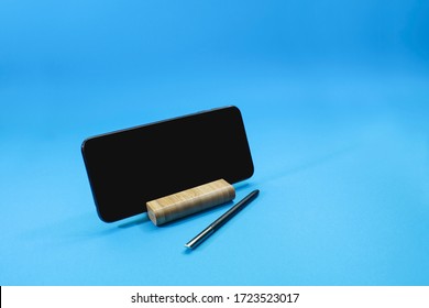 View Of A Smart Phone On The Desk Holder With An Electronic Pen Isolated On Blue Background.  Information And Technology Concept