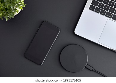 View of smartphone, laptop and wireless charger laying on grey office desk from directly above. Modern technology, wireless device and transfer of energy concept.