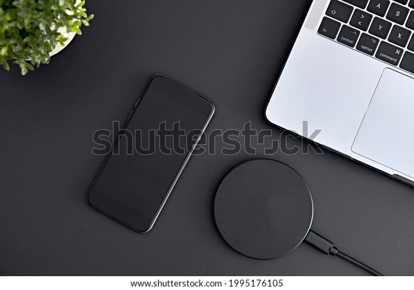 View of smartphone, laptop\
and wireless charger laying on grey office desk from directly\
above. Modern technology, wireless device and transfer of energy\
concept.