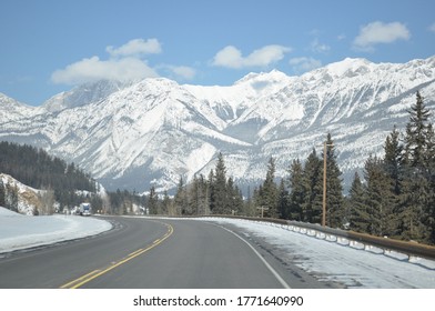 View Of The Snow Covered Rocky Mountains From The Highway, With A Bend In The Road Ahead.