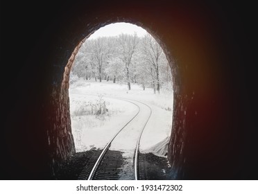 View of snow covered trees from inside a dark railway tunnel