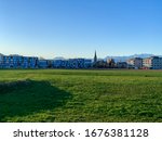 View of the snowed swiss alps mountains with the Wetzikon Church in the middle and a grass field in front during a beautiful sunny day of spring