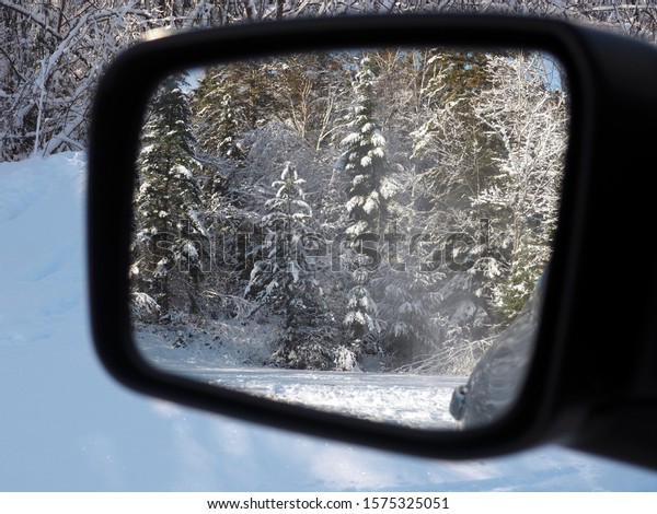 View of snowy forest in the car\'s driver\'s mirror.\
Small snow blow flying in the air. Taken end November in Michigan\'s\
Upper Peninsula (USA).
